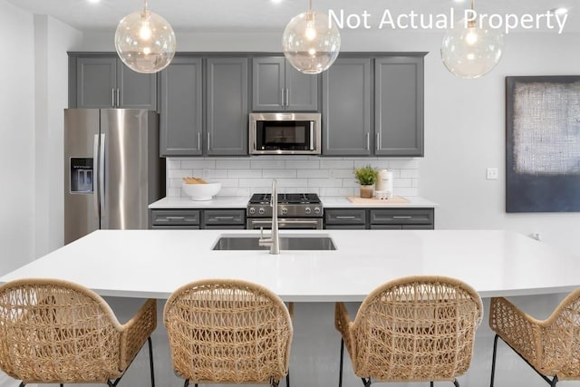 kitchen featuring decorative backsplash, sink, hanging light fixtures, appliances with stainless steel finishes, and gray cabinetry