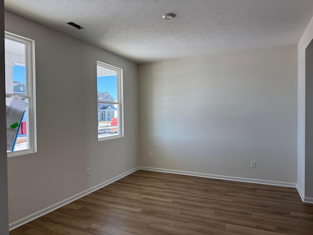 empty room featuring a textured ceiling, dark hardwood / wood-style floors, and a healthy amount of sunlight