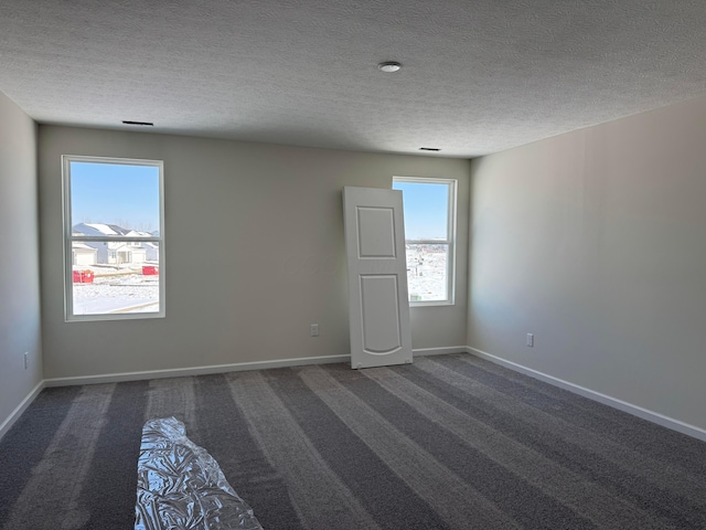 unfurnished room featuring a textured ceiling and dark colored carpet