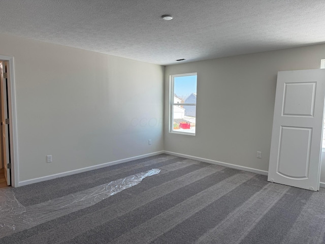 spare room featuring a textured ceiling and dark colored carpet