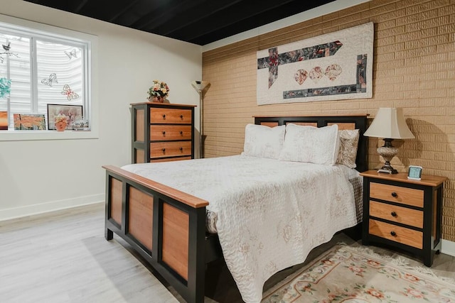 bedroom featuring brick wall and light hardwood / wood-style floors