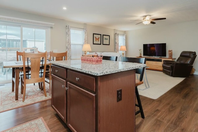 kitchen featuring a kitchen bar, dark hardwood / wood-style flooring, light stone counters, ceiling fan, and a center island