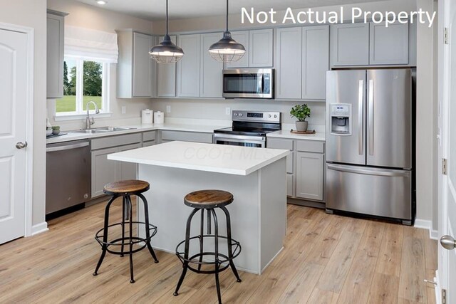 kitchen featuring a breakfast bar, a center island, gray cabinets, stainless steel appliances, and a sink