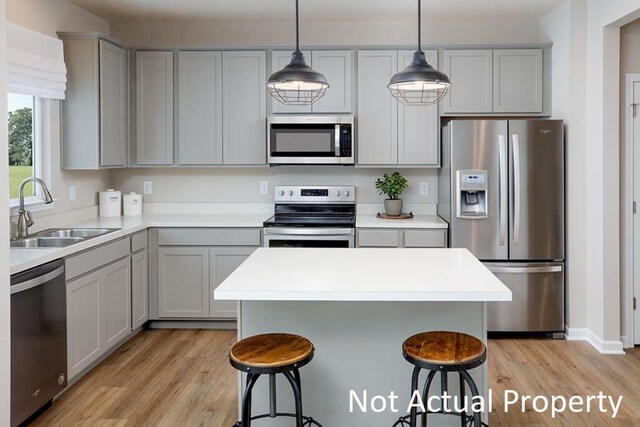 kitchen featuring light wood finished floors, a kitchen breakfast bar, stainless steel appliances, gray cabinetry, and a sink