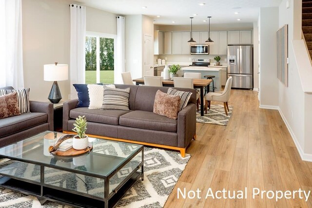 living room featuring light wood-style floors, stairway, baseboards, and recessed lighting