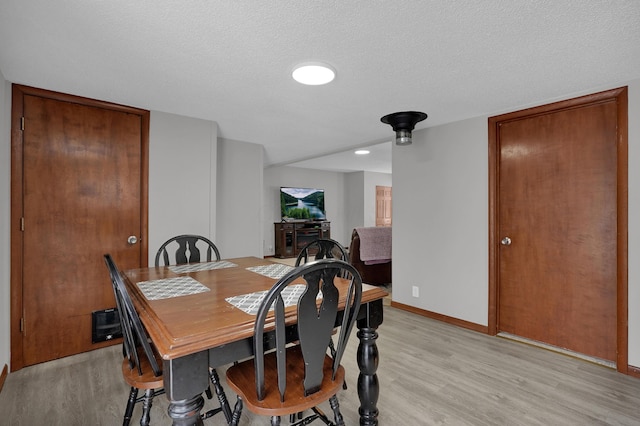 dining room featuring light wood-type flooring and a textured ceiling