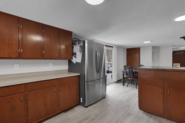 kitchen with a textured ceiling, light hardwood / wood-style floors, and stainless steel refrigerator