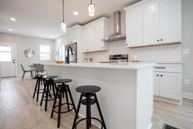 kitchen featuring white cabinets, an island with sink, pendant lighting, and wall chimney range hood