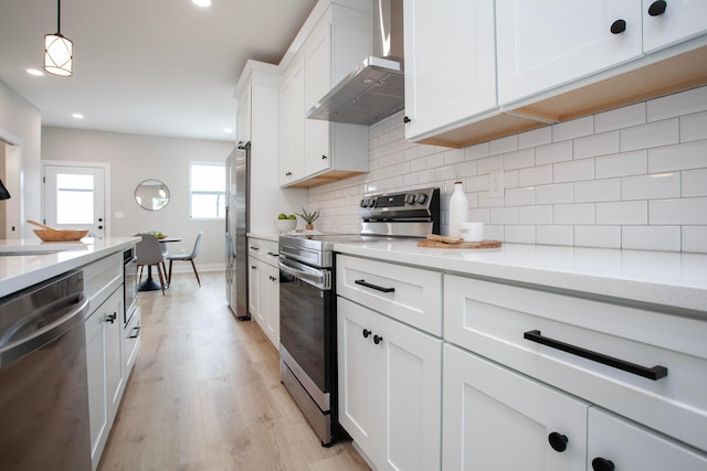 kitchen with wall chimney range hood, light wood-type flooring, decorative light fixtures, white cabinetry, and stainless steel appliances