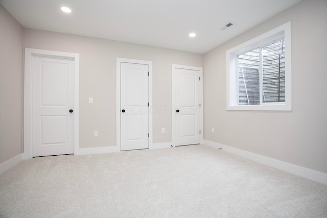 unfurnished bedroom featuring light carpet and two closets