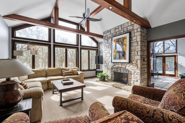 carpeted living room with beam ceiling, ceiling fan, a stone fireplace, high vaulted ceiling, and baseboards