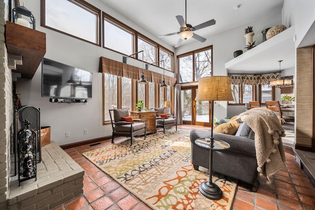 tiled living area with ceiling fan with notable chandelier, a high ceiling, and baseboards