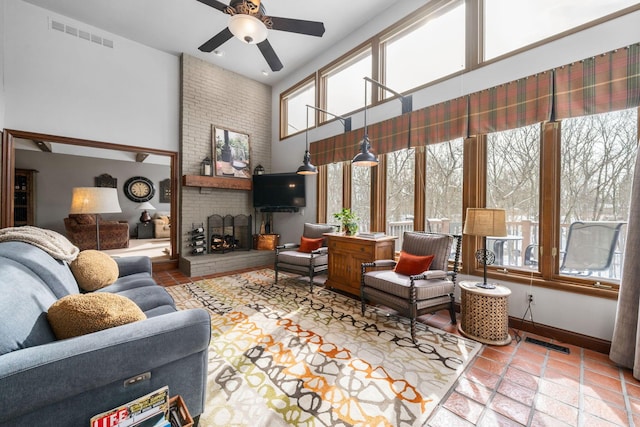 living area with a high ceiling, a brick fireplace, visible vents, and baseboards