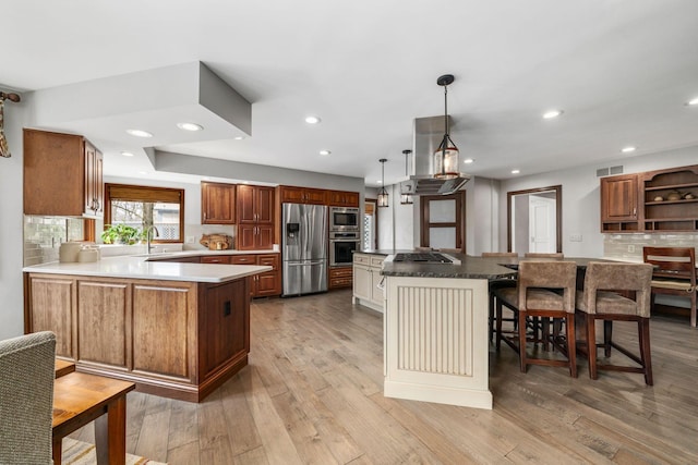 kitchen with stainless steel appliances, visible vents, a sink, light wood-type flooring, and a peninsula