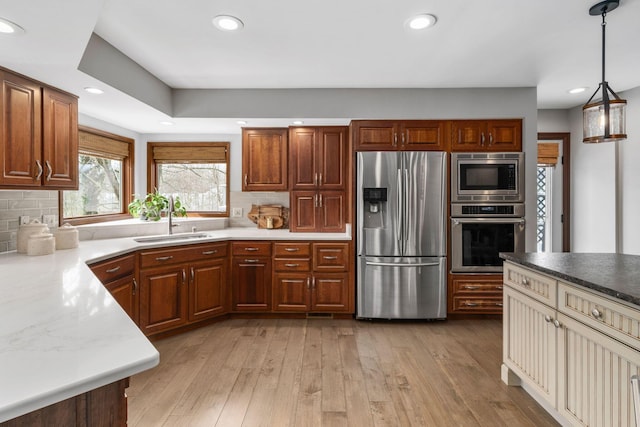 kitchen with stainless steel appliances, light wood-type flooring, a sink, and decorative backsplash