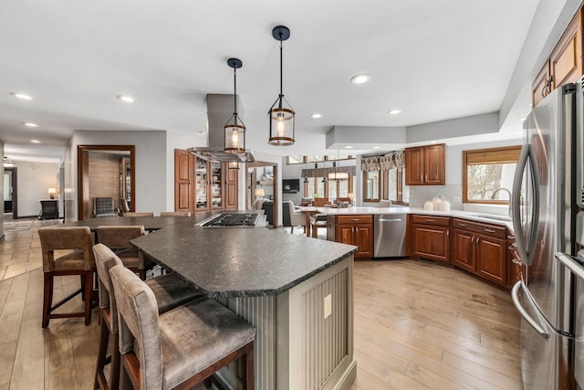 kitchen with a breakfast bar area, island range hood, a peninsula, appliances with stainless steel finishes, and light wood finished floors