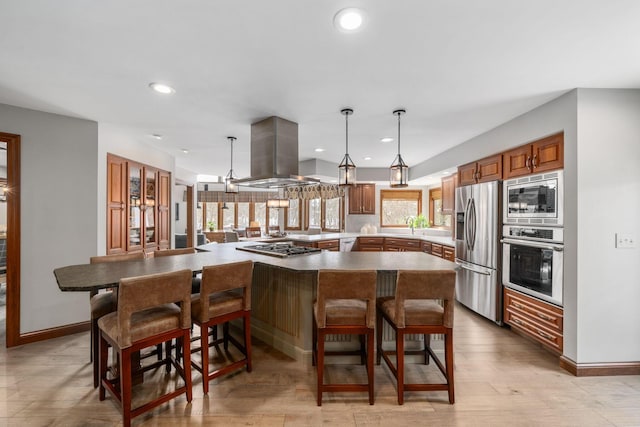 kitchen with island exhaust hood, recessed lighting, appliances with stainless steel finishes, brown cabinetry, and a kitchen bar