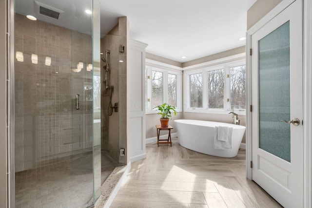 full bathroom with a stall shower, a freestanding tub, visible vents, and baseboards