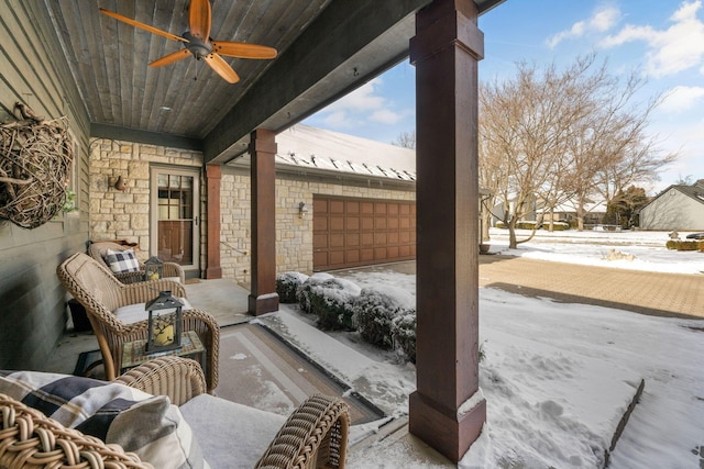 snow covered patio featuring ceiling fan and an attached garage