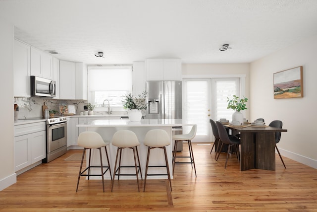 kitchen with white cabinets, stainless steel appliances, a kitchen island, and light hardwood / wood-style floors