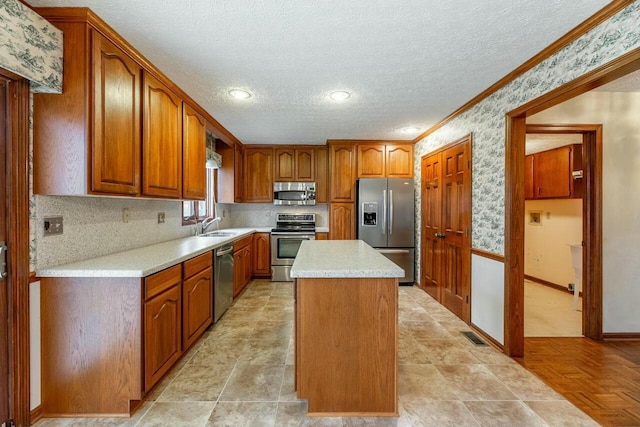 kitchen with sink, ornamental molding, a textured ceiling, a kitchen island, and stainless steel appliances