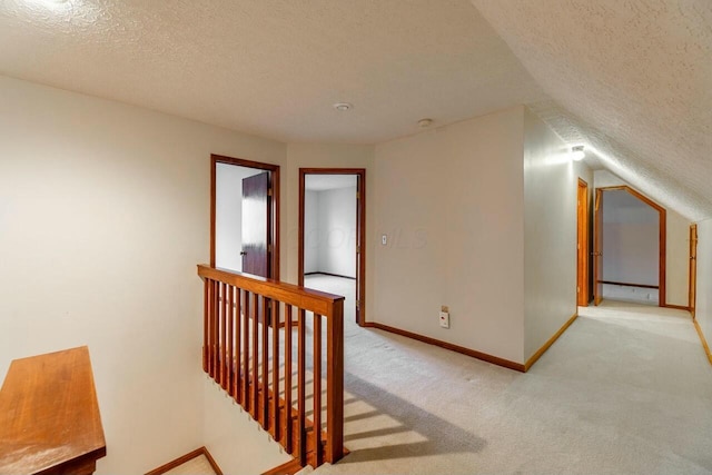 hall featuring a textured ceiling, light colored carpet, and vaulted ceiling