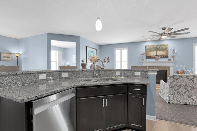 kitchen with sink, light hardwood / wood-style flooring, stainless steel dishwasher, a fireplace, and light stone counters