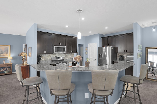 kitchen with dark brown cabinets, hanging light fixtures, appliances with stainless steel finishes, kitchen peninsula, and carpet