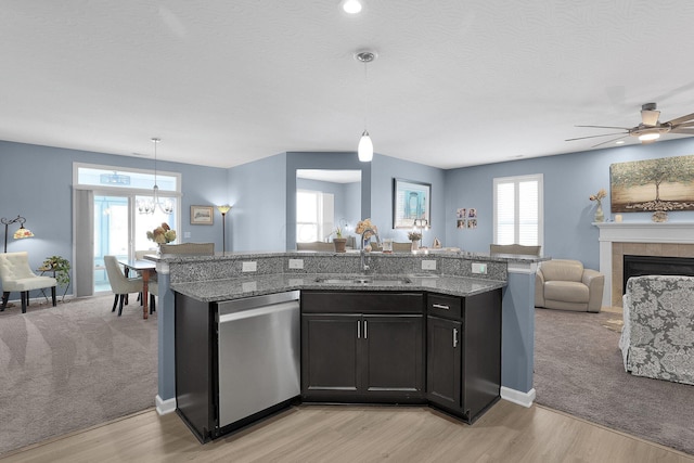 kitchen with pendant lighting, dishwasher, sink, light stone countertops, and a tiled fireplace