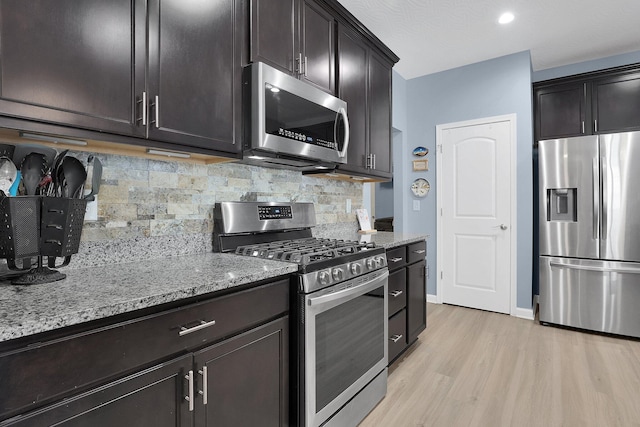 kitchen with dark brown cabinets, backsplash, appliances with stainless steel finishes, and light hardwood / wood-style flooring