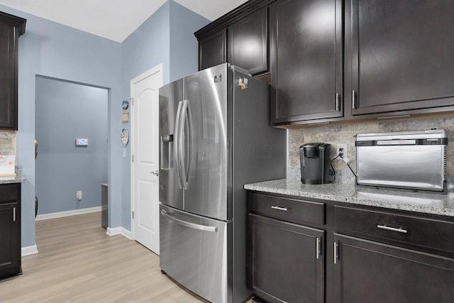 kitchen with tasteful backsplash, stainless steel refrigerator with ice dispenser, light stone countertops, dark brown cabinets, and light hardwood / wood-style flooring