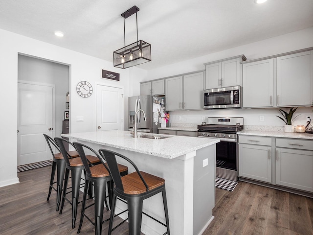 kitchen featuring an island with sink, appliances with stainless steel finishes, gray cabinetry, dark hardwood / wood-style flooring, and hanging light fixtures