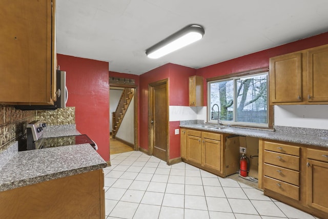 kitchen with decorative backsplash, light tile patterned flooring, stove, and sink