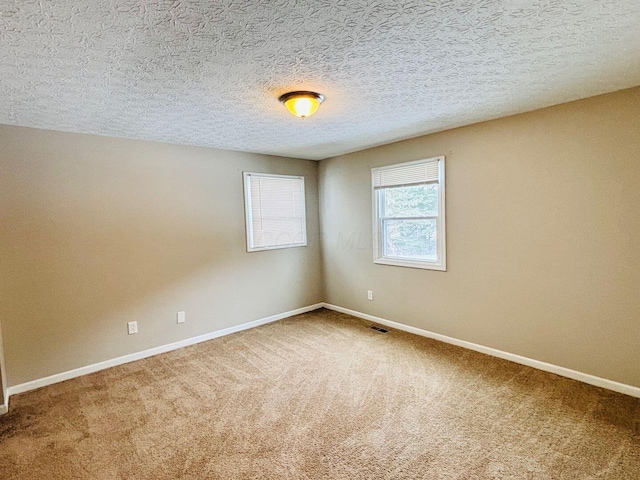 unfurnished room with visible vents, a textured ceiling, baseboards, and carpet