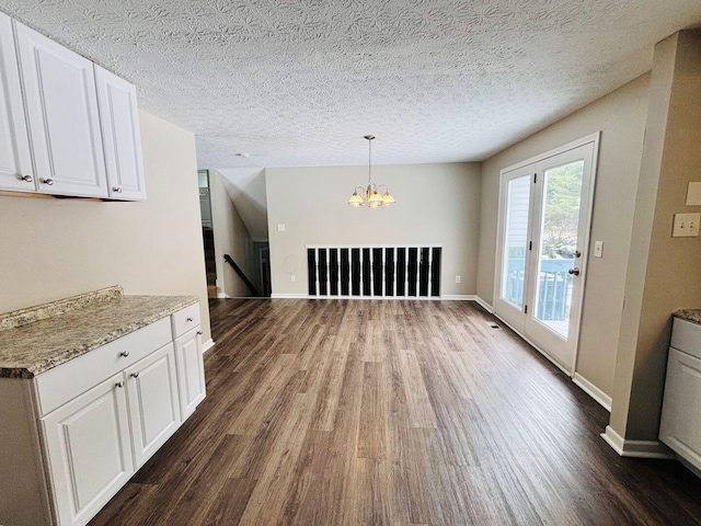 unfurnished dining area with a textured ceiling, wood finished floors, baseboards, and a chandelier