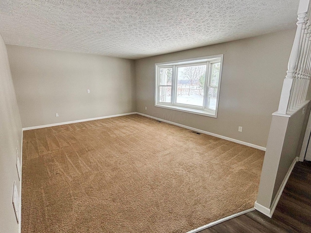 carpeted spare room with visible vents, baseboards, and a textured ceiling