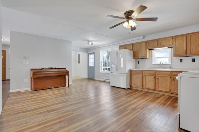 kitchen featuring stove, white refrigerator with ice dispenser, sink, ceiling fan, and light wood-type flooring