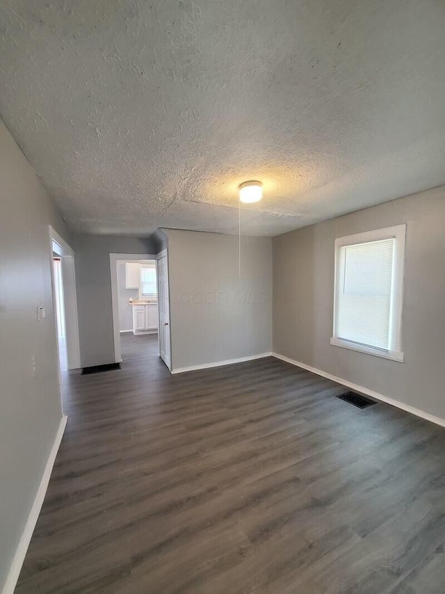 spare room with a textured ceiling, plenty of natural light, and dark hardwood / wood-style floors