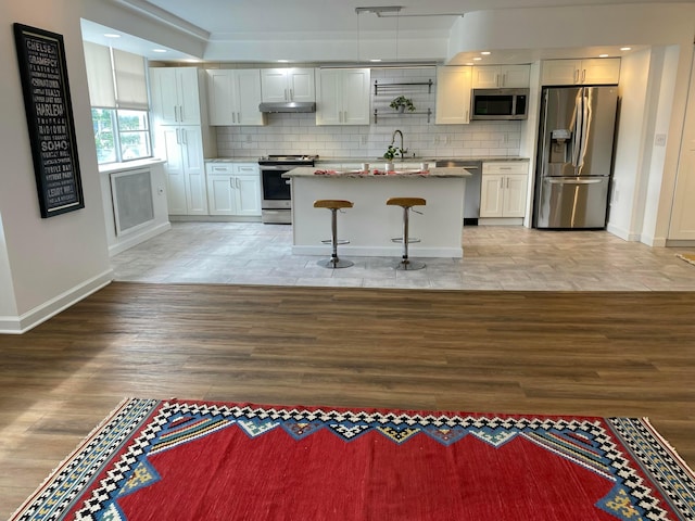 kitchen with appliances with stainless steel finishes, light wood-type flooring, tasteful backsplash, a breakfast bar, and white cabinetry