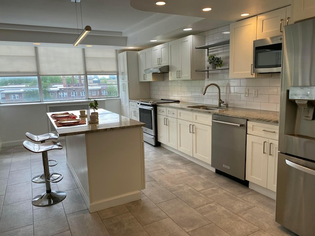 kitchen featuring appliances with stainless steel finishes, white cabinetry, sink, a center island, and light stone counters