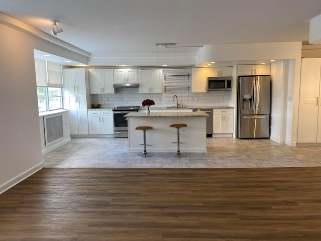 kitchen with a breakfast bar area, light stone counters, white cabinetry, pendant lighting, and stainless steel appliances