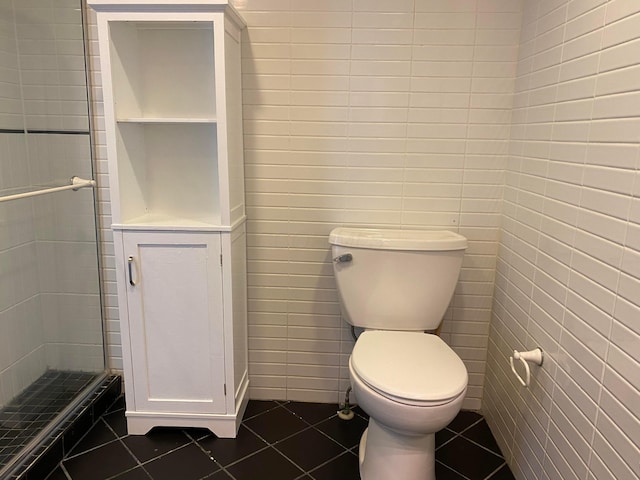 bathroom with tile patterned flooring, toilet, tile walls, and a shower with shower door