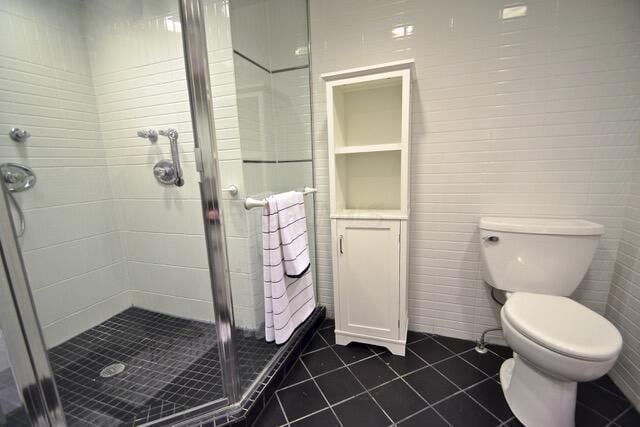 bathroom featuring tile patterned floors, a shower with door, and toilet