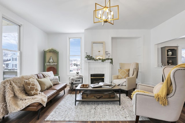 living room featuring a tiled fireplace, a healthy amount of sunlight, dark hardwood / wood-style flooring, and a chandelier