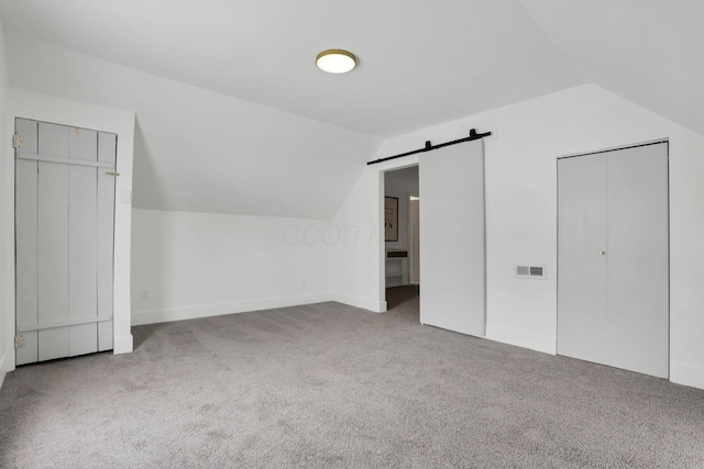 additional living space with a barn door, light colored carpet, and lofted ceiling