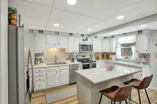 kitchen featuring a kitchen island, appliances with stainless steel finishes, white cabinetry, sink, and a kitchen bar