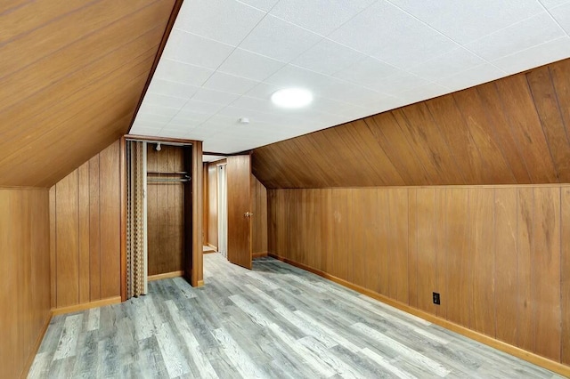 additional living space with lofted ceiling, light hardwood / wood-style flooring, and wood walls