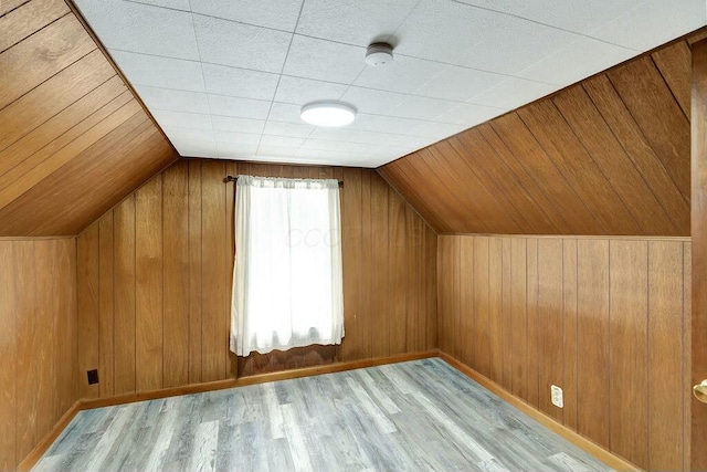 additional living space with wood walls, vaulted ceiling, and light wood-type flooring