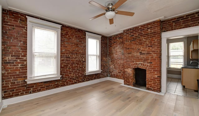 unfurnished living room with ornamental molding, brick wall, ceiling fan, a fireplace, and light hardwood / wood-style floors