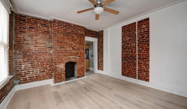 unfurnished living room featuring a brick fireplace, ceiling fan, light wood-type flooring, ornamental molding, and brick wall